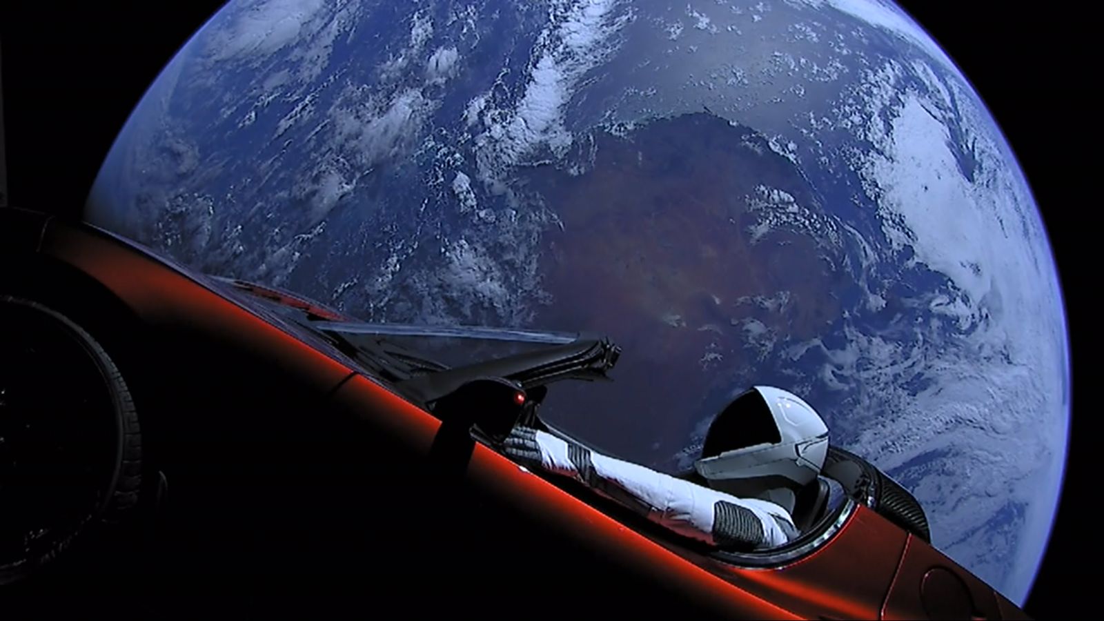 Starman, a mannequin in a SpaceX spacesuit, at the wheel of Elon Musk's red Tesla Roadster with Earth behind it
