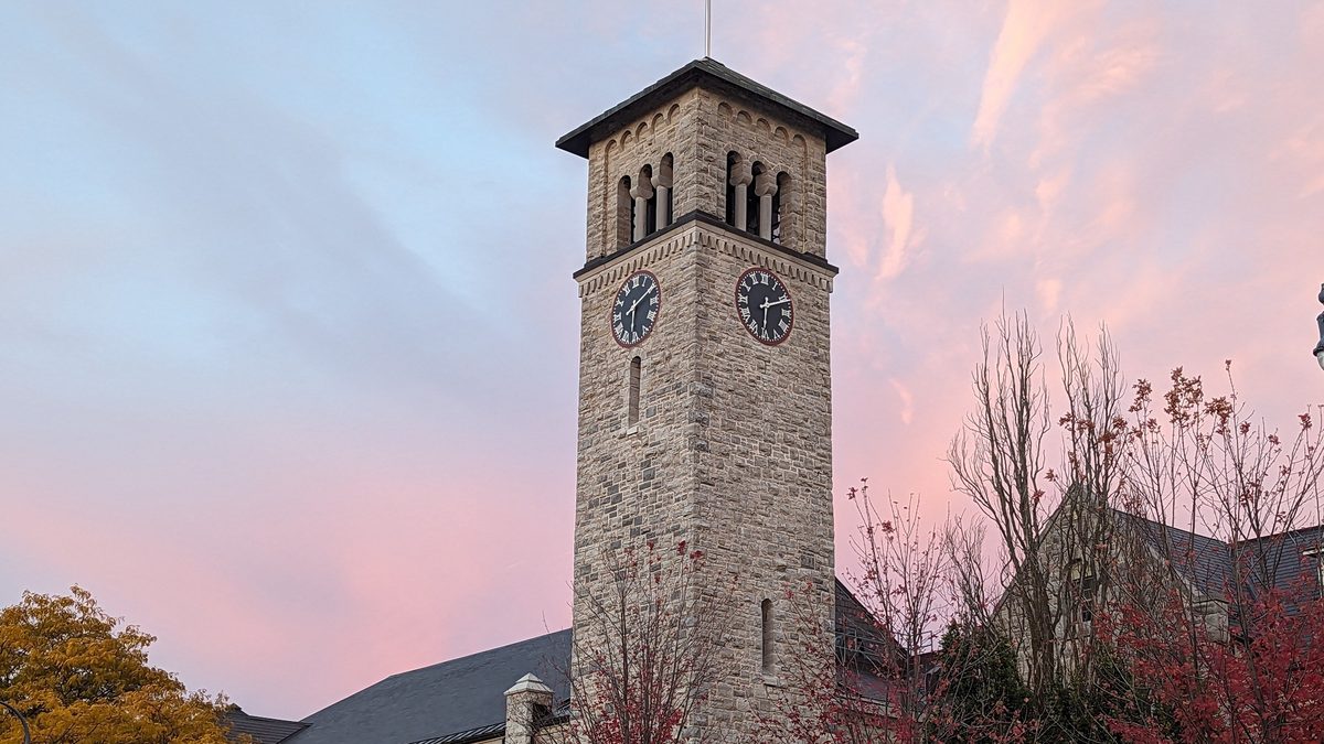 The stone clock tower of Grant Hall at Queen's University in Kingston, Ontario, under a pink sky