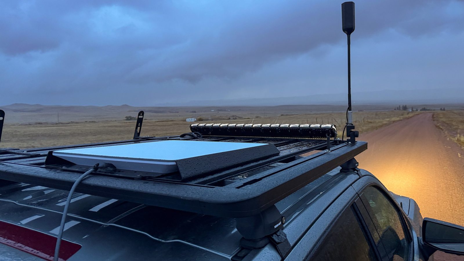 Starlink flat-panel dish mounted on the roof rack of a truck on a rural dirt road
