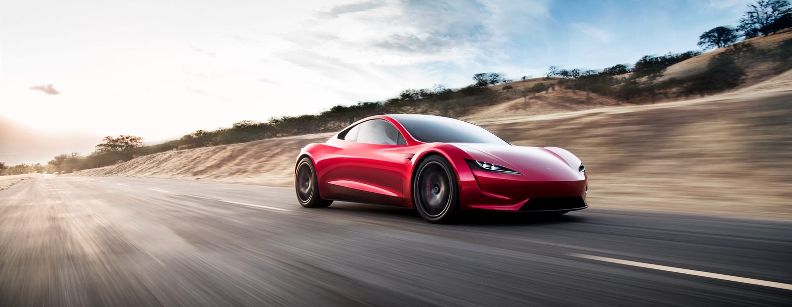 A red Tesla Roadster at speed on an open road