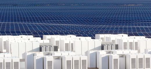 Rows of white Tesla Megapacks in front of a large field of blue solar panels
