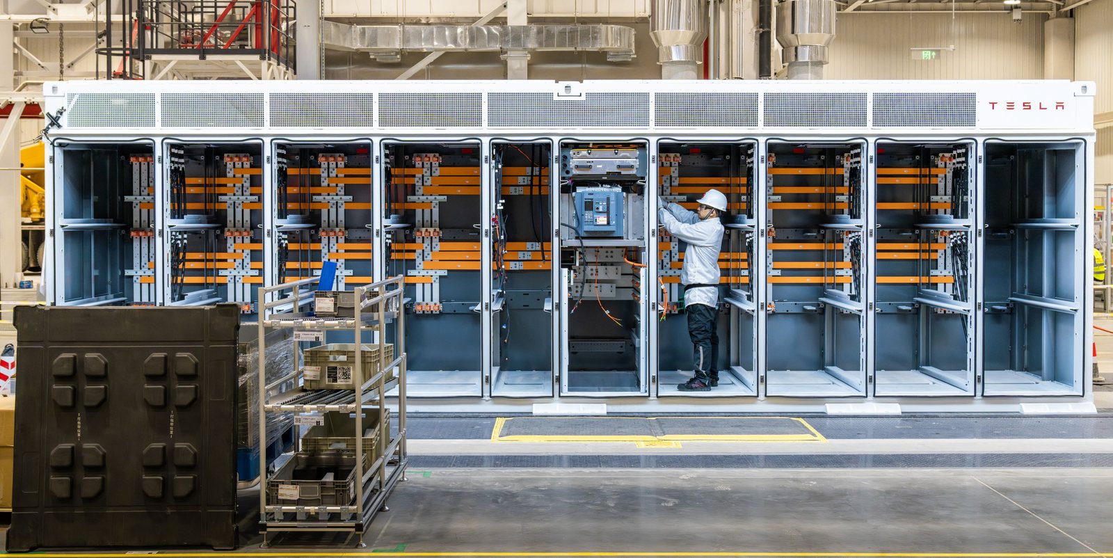 Tesla Megapack with front panels open, showing busbars and a technician at work