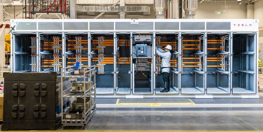 Tesla Megapack with front panels open, showing busbars and a technician at work