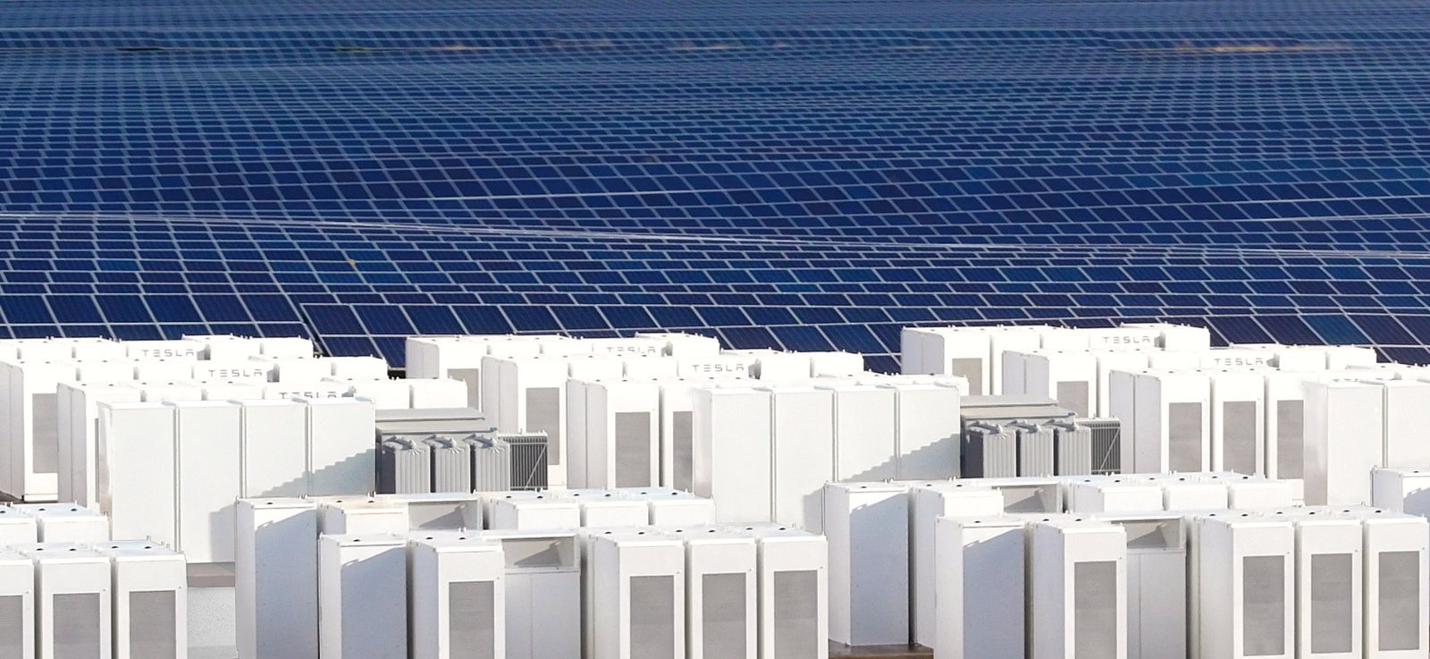 Rows of white Tesla Megapacks in front of a large field of blue solar panels