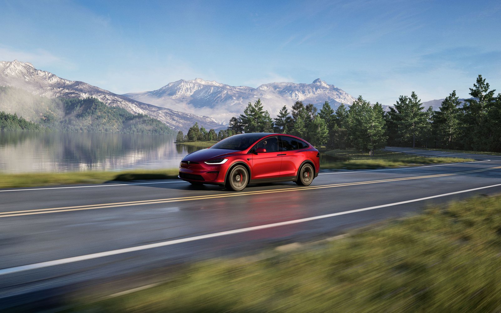 Tesla Model X in Ultra Red driving on a lakeside road with snow-capped mountains
