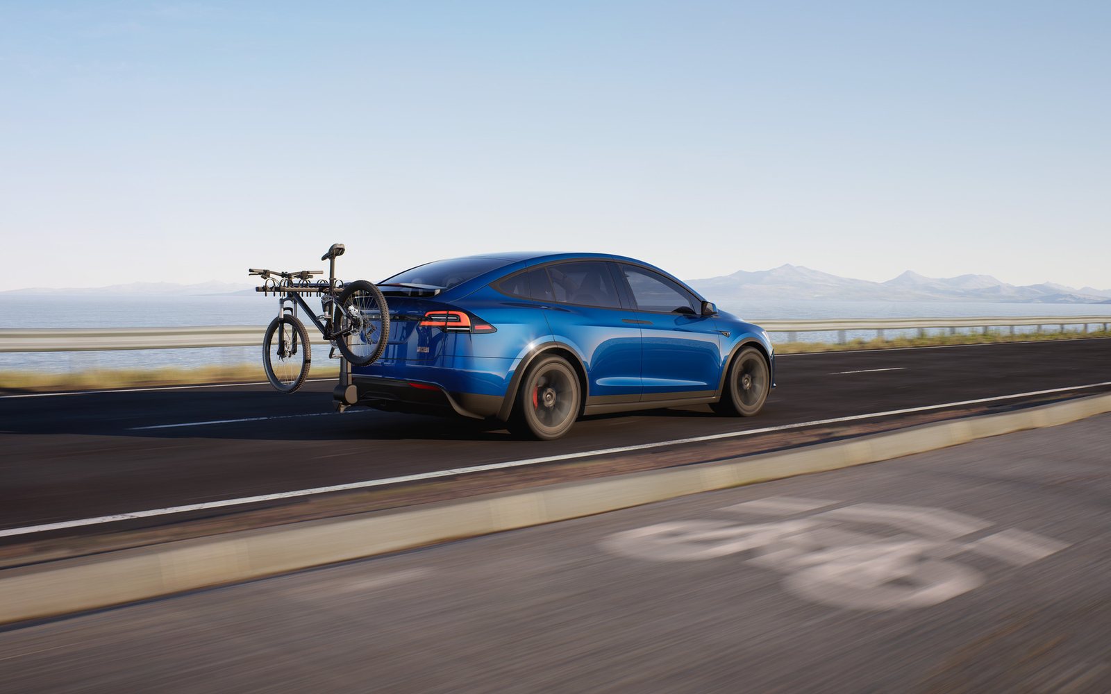 Blue Tesla Model X on a coastal road with a mountain bike on a hitch rack