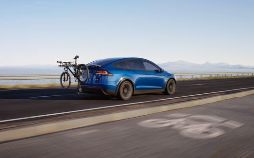 Blue Tesla Model X on a coastal road with a mountain bike on a hitch rack