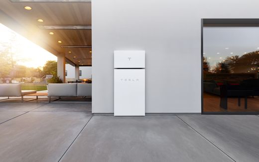 White Tesla Powerwall mounted on a modern home patio wall at sunset