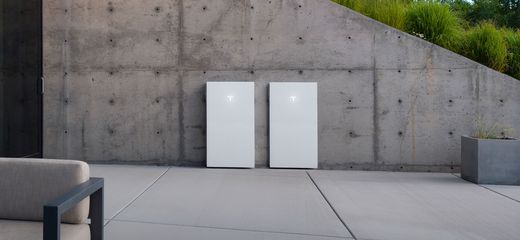 Two Tesla Powerwall units with glowing T logos mounted on a concrete patio wall
