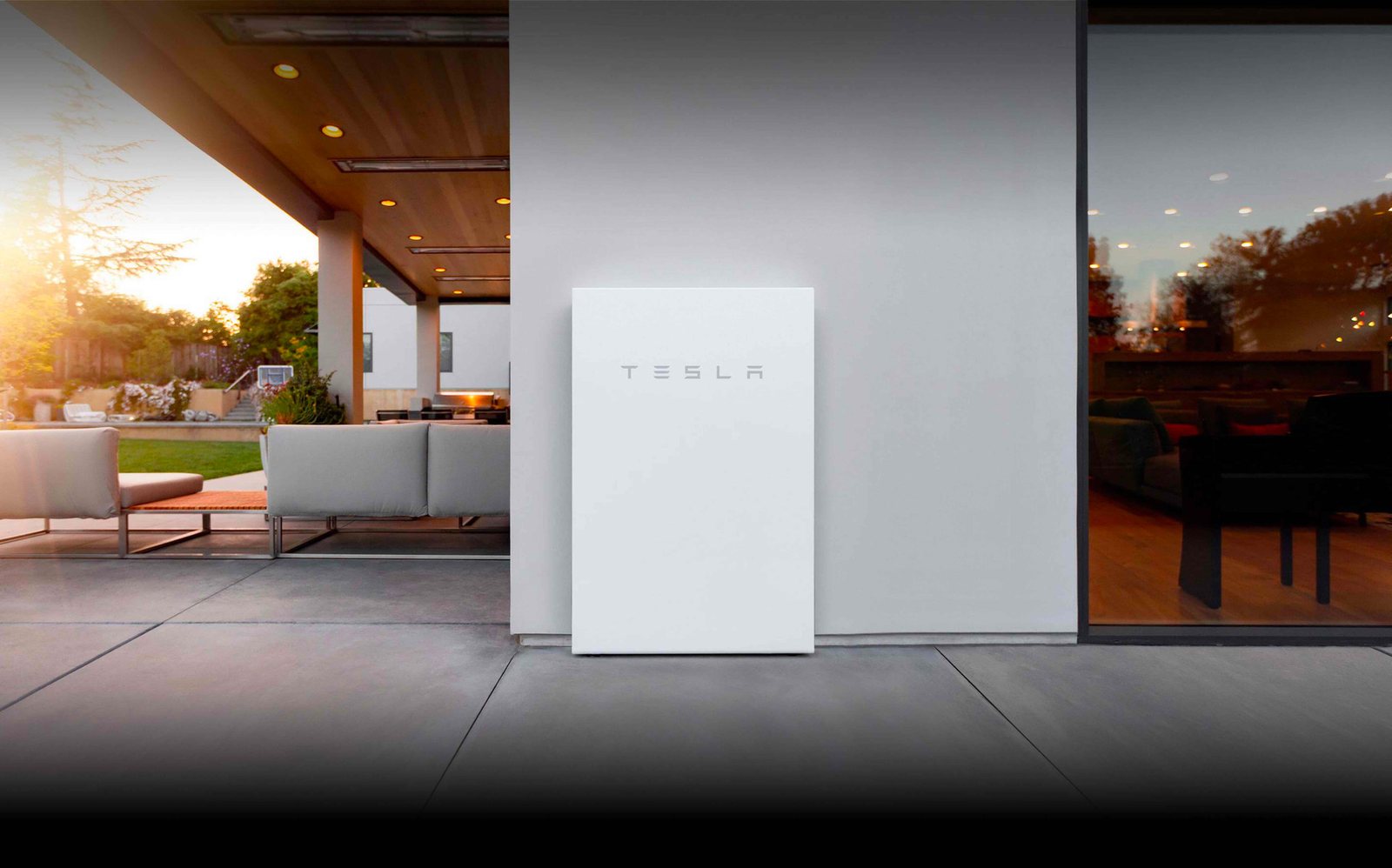 Tesla Powerwall installed on a white house wall beside a dusk patio lounge