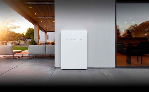 Tesla Powerwall installed on a white house wall beside a dusk patio lounge