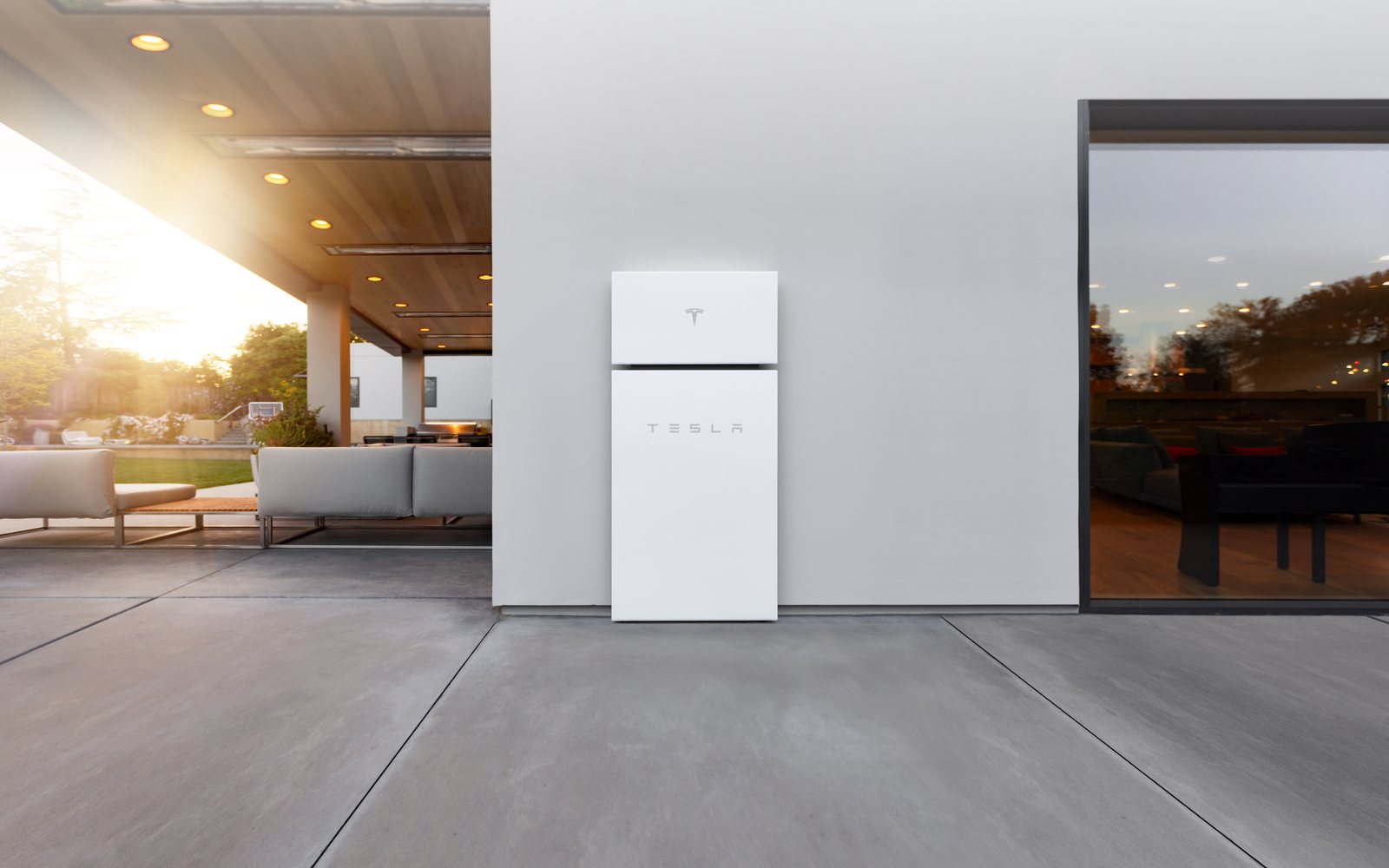 White Tesla Powerwall mounted on a modern home patio wall at sunset