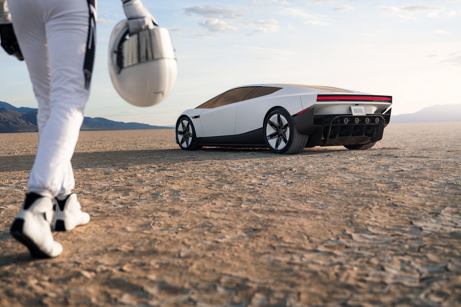 A driver in a white suit carrying a helmet walks toward the white 2026 Tesla Roadster on a dry lakebed