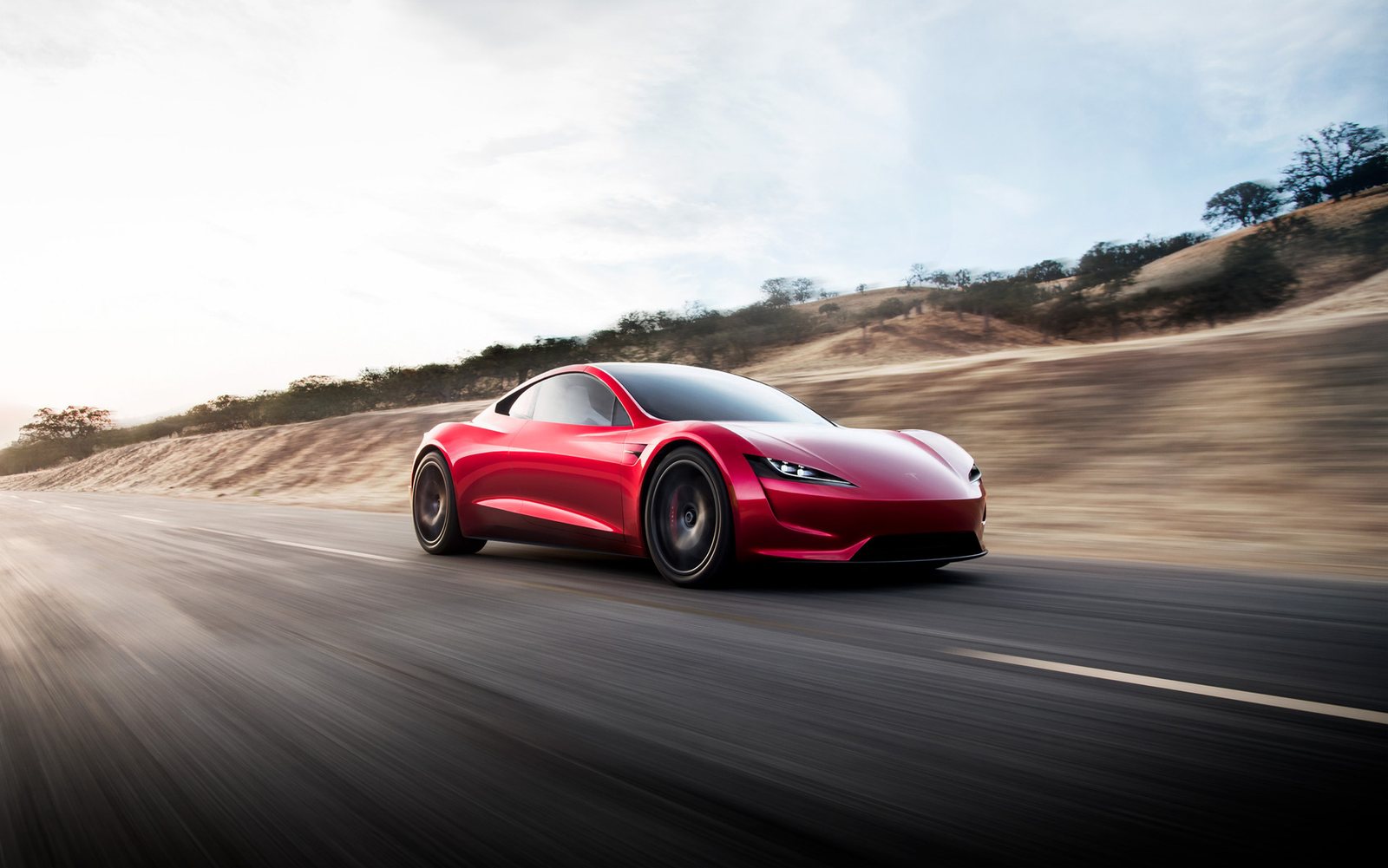 Red next-generation Tesla Roadster driving at speed on a dry hillside road