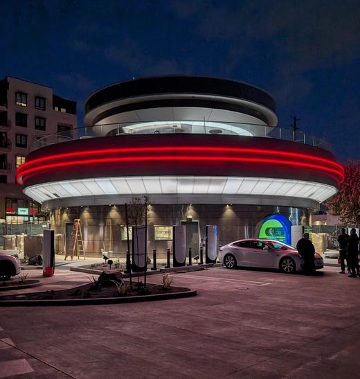 Tesla Diner Supercharger at night with a circular neon-lit building and a Model 3 charging