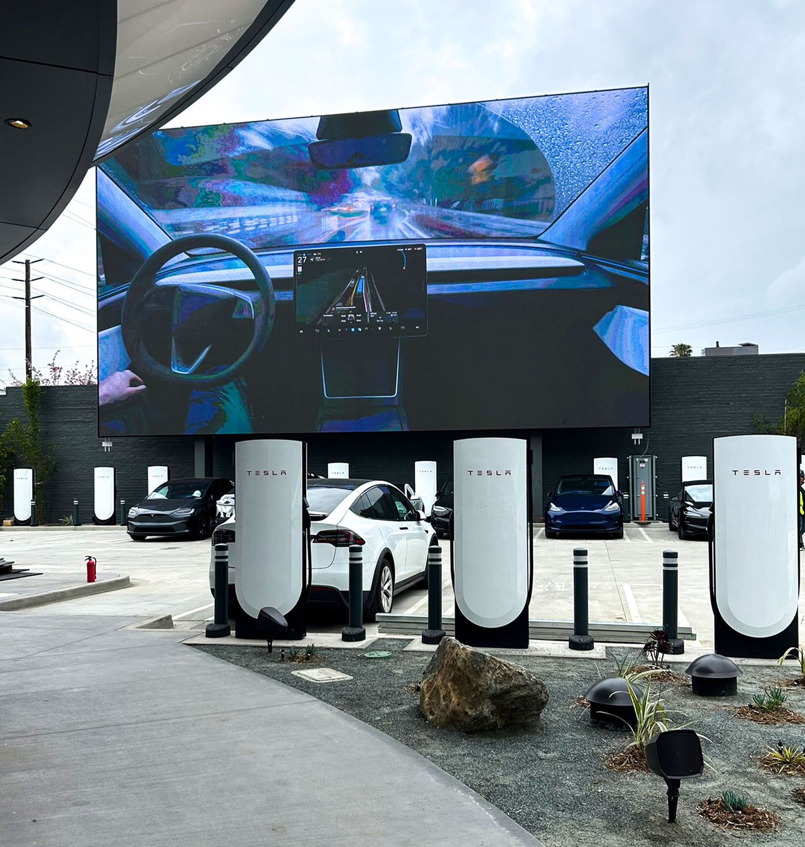 Hollywood Tesla Supercharger with a giant outdoor screen and vehicles at V4 stalls