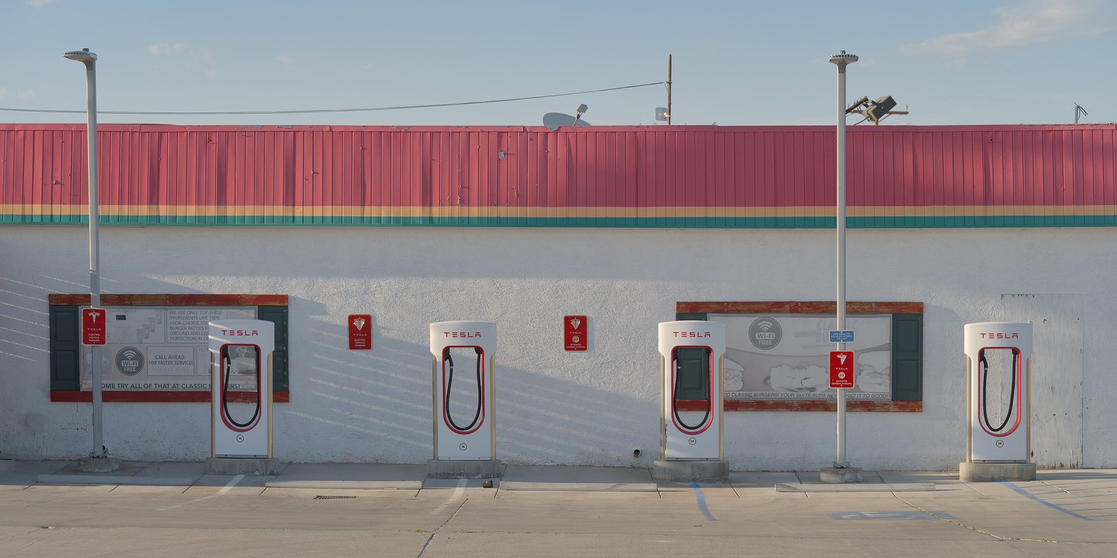 Four Tesla Supercharger stalls in front of a white building with a red roof in Inyokern, California