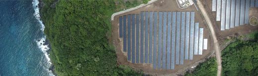 Aerial view of a Tesla solar array on a coastal cliff beside forest and ocean