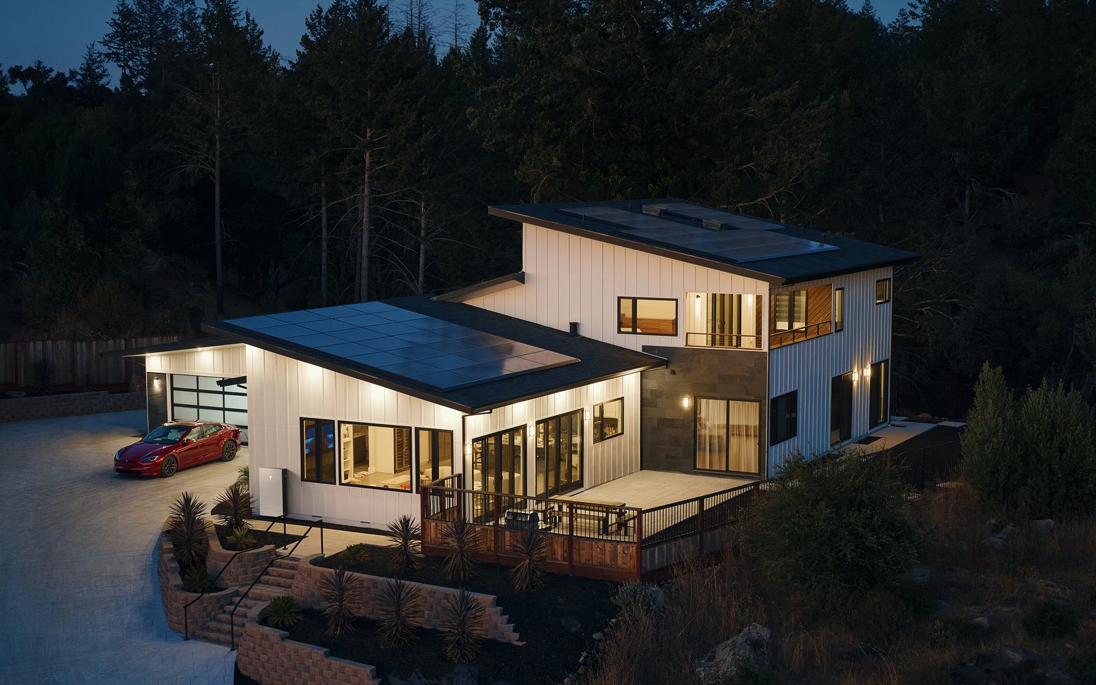 Tesla home solar installation at dusk on a modern hillside house with a red Model S